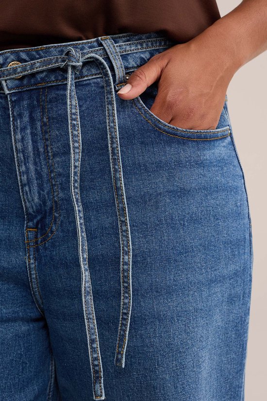 Detail van een wijde spijkerbroek met strikceintuur en steekzak.
