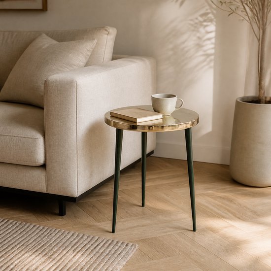 Table d'appoint ronde avec plateau doré et pieds vert foncé, à côté d'un canapé beige.
