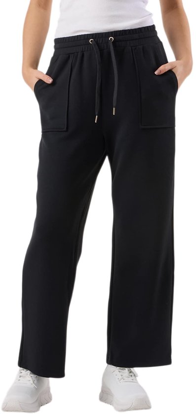Model in een zwarte, wijde joggingbroek met tunnelkoord en opgestikte zakken, en witte sneakers.