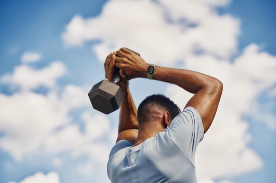 Man tilt gewicht boven zijn hoofd, met een olijfgroene Fitbit Edge smartwatch om zijn pols.