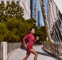 Vrouw in bordeauxrode sportkleding jogt op een stadsbrug met Fitbit Edge om de pols.