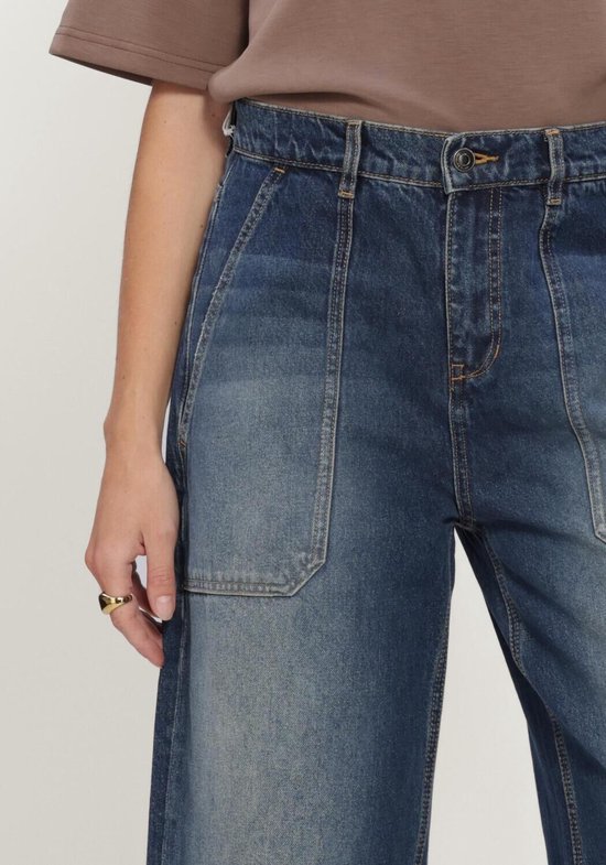 Detail van de wijde jeans in donkerblauw denim, met opgestikte zakken aan de voorkant.
