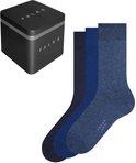 Drie paar blauwe Falke Happy sokken in gradaties van donker naar licht, naast een zwarte metalen Falke geschenkdoos.