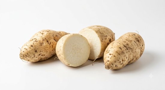 Twee hele en twee doorgesneden witte zoete aardappelen met een lichtbruine schil, liggend op een witte ondergrond.