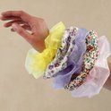 Hand met een verzameling kleurrijke scrunchies van organza en bloemenstof.