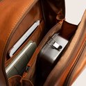 Binnenkant van een bruine leren rugzak met een tablet, notitieblok en metalen broodtrommel.
