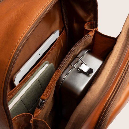 Binnenkant van een bruine leren rugzak met een tablet, notitieblok en metalen broodtrommel.