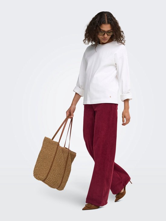 Model dat loopt in bordeauxrode corduroy broek met wijde pijpen, witte top en bruine tas.