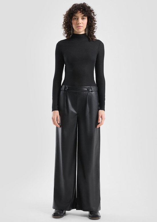 Model draagt een zwarte, wide-leg broek van imitatieleer gecombineerd met een zwarte coltrui.