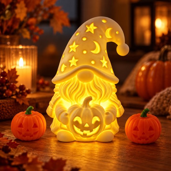 Lutin lumineux avec étoiles et lunes découpées sur le bonnet, assis avec deux petites citrouilles sur une table en bois.