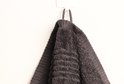 Donkergrijze handdoek met ribbeltextuur, hangend aan een haakje aan de muur.