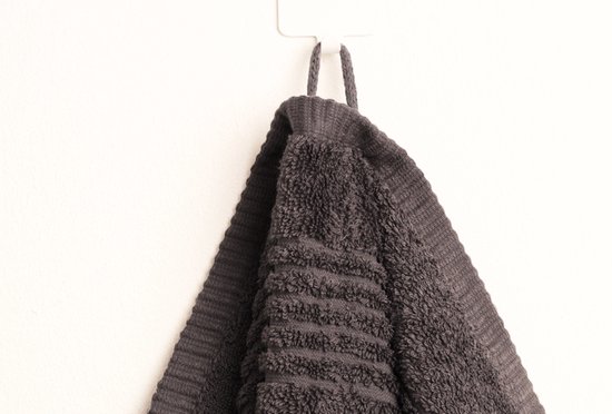 Donkergrijze handdoek met ribbeltextuur, hangend aan een haakje aan de muur.