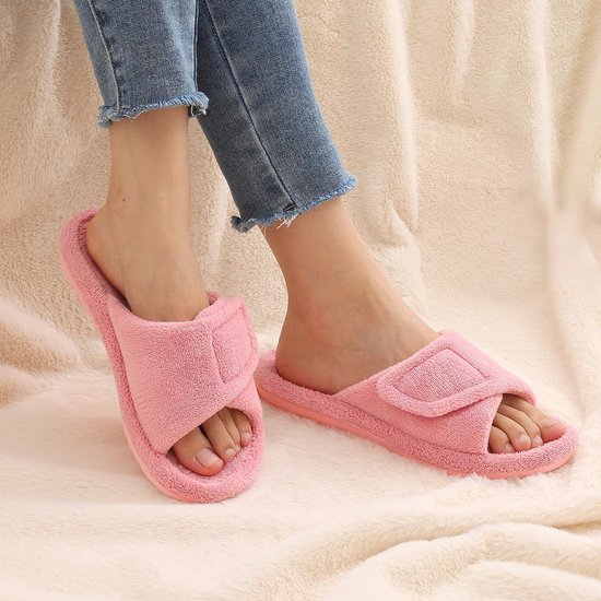 Roze badstof slippers met verstelbare klittenbandsluiting aan de voeten van een model met spijkerbroek.