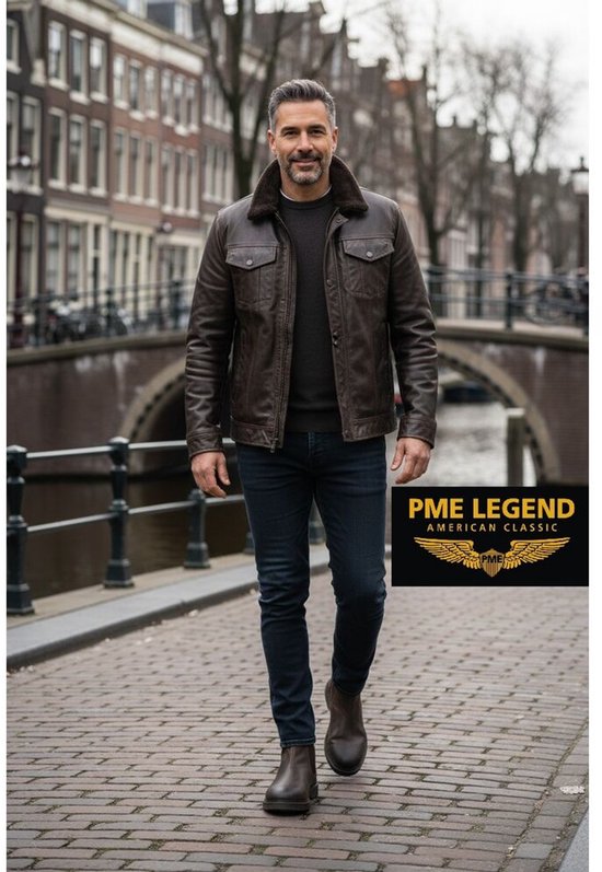 Model draagt een bruine jas over een donkere trui met jeans en bruine Chelsea boots.