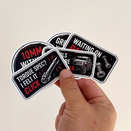 Hand houdt een verzameling van vijf verschillende zwarte vinylstickers met autothema vast.