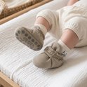 Baby voeten omhoog op aankleedkussen, draagt taupe Steppies slofjes met antislip-zool.