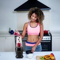Vrouw in sportkleding vult een zwarte Zenvox 1200W blender met verse frambozen in de keuken.