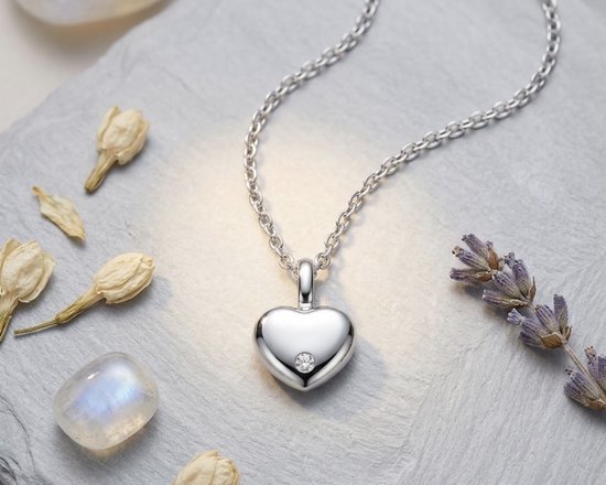 Zilverkleurige hartvormige hanger aan een ketting met een centraal ingezet diamantje op een stenen ondergrond.