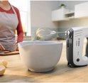 Witte en grijze Bosch ErgoMixx handmixer van 750W boven een mengkom met beslag, op een houten keukenblad.