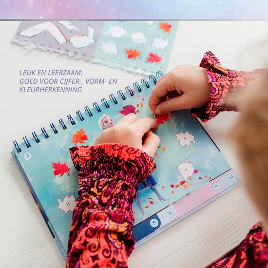 Enfant en chemisier coloré collant des autocollants de feuilles d'automne par numéro dans un cahier La Reine des Neiges.