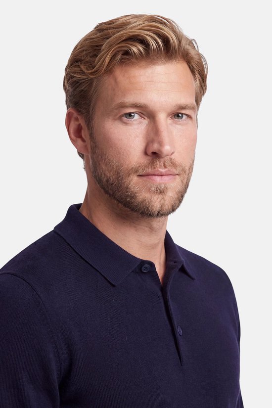 Close-up van een man met blond haar en een donkerblauwe polo met kraag.