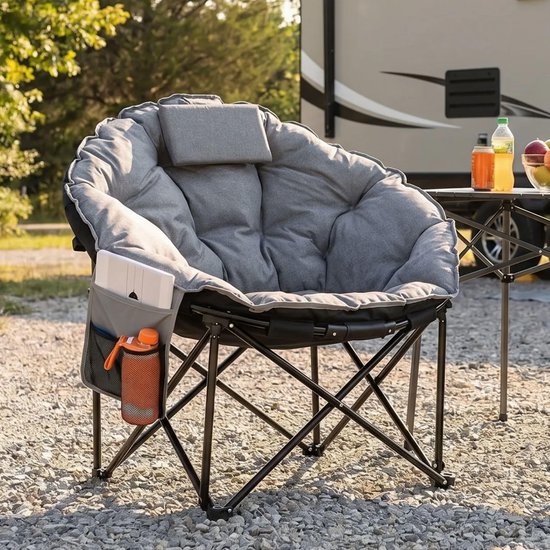Grijze, gewatteerde ronde campingstoel met kussen en opbergvak, staand op grind bij een camper.