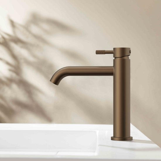 STRIA wastafelkraan in geborsteld bruin brons op een witte wastafel met een decoratieve schaduw op de muur.