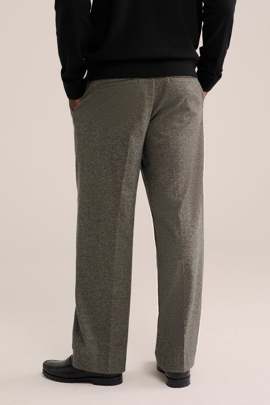 Achteraanzicht van een model in een grijze loose fit broek met achterzakken en zwarte schoenen.