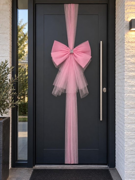 XL roze tule strik met glitter hartje, bevestigd aan een zwarte deur.