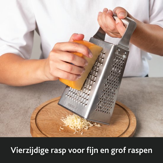 Een hand wordt gebruikt om een stuk kaas over een roestvrijstalen, vierzijdige rasp te wrijven.