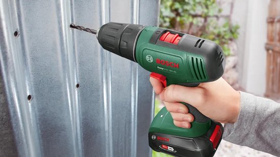 Hand boort met de groene Bosch EasyDrill 18V-40 in een metalen wand.