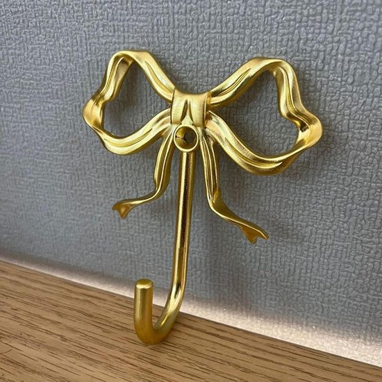 Eén goudkleurige strikhaak gemonteerd op een grijze wand met houten afwerking.