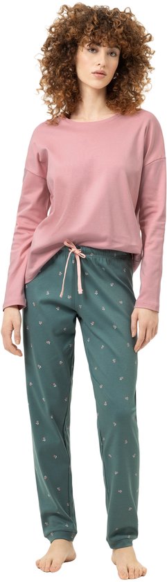 Model draagt een roze shirt met lange mouwen en een donkergroene broek met kleine bloemetjes.