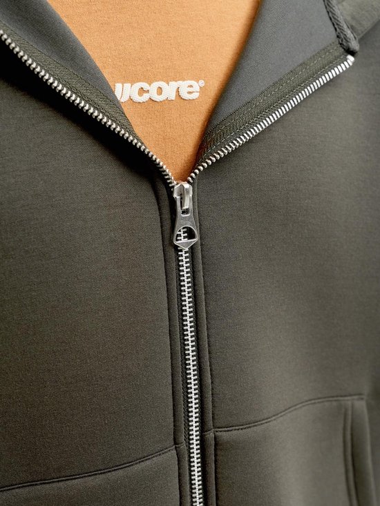 Close-up van een donkergroene hoodie met ritssluiting en een oranje T-shirt eronder met de tekst "score".