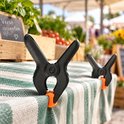 Zwarte marktklemmen met oranje bekleding op een tafel met groen-wit gestreepte tafelkleed. "Verse groenten" staat op een krijtbord.