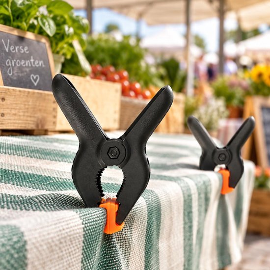 Zwarte marktklemmen met oranje bekleding op een tafel met groen-wit gestreepte tafelkleed. "Verse groenten" staat op een krijtbord.