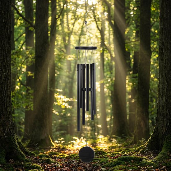 Zwarte metalen windgong hangend in een zonnig bos, omgeven door bomen en mos.