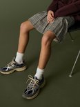 Detailopname van een geplooide rok met ruitpatroon en sneakers op een groene achtergrond.