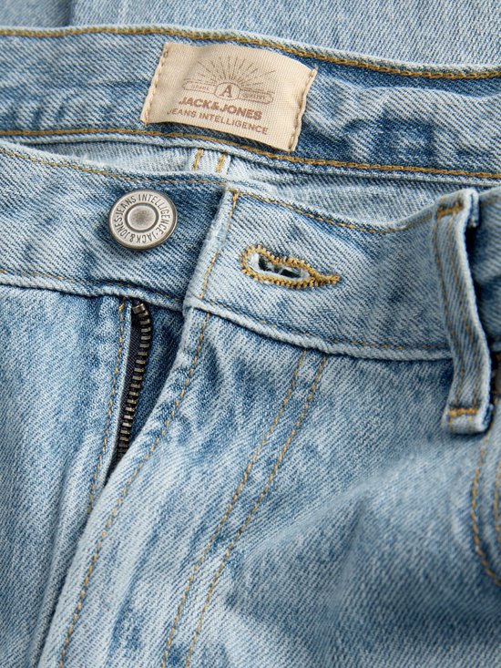 Close-up van de gulp en knoop van een lichtblauwe spijkerbroek met 'JACK & JONES JEANS INTELLIGENCE' op de knoop.