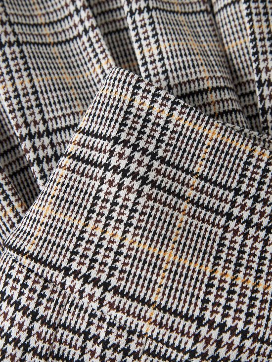 Close-up van de geplooide stof van een rok met een grijs, zwart en bruin ruitpatroon.