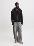Model draagt een zwart scuba-vest met capuchon, grijze wijde jeans en beige sneakers.