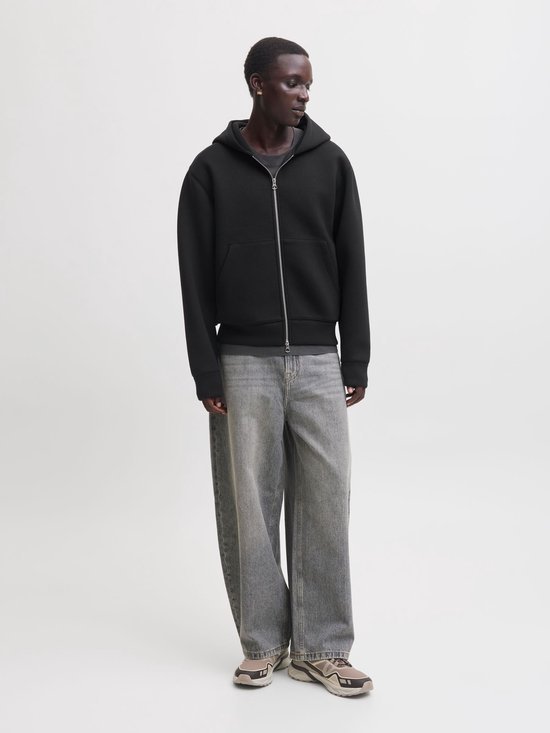 Model draagt een zwart scuba-vest met capuchon, grijze wijde jeans en beige sneakers.
