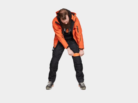 Man met baard in oranje jas en zwarte werkbroek die oranje Herock kniebeschermers in de broekzak plaatst.