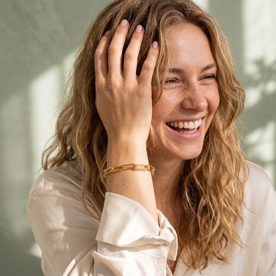 Lachende vrouw met krullend haar draagt een goudkleurige schakelarmband om haar pols.