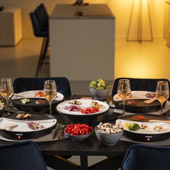 Eettafel gedekt voor gourmetten, met vier gourmetstellen, borden met zalm, burger, groenten en glazen witte wijn.