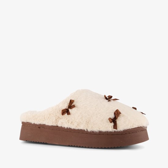 Schuin zijaanzicht van een crèmekleurige pantoffel met bruine strikjes en een bruine platformzool.