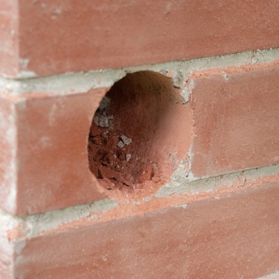 Een rond gat in een rode bakstenen muur, voorbereid voor een boor.