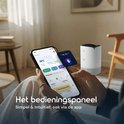 Handen houden een smartphone met de Vibrix app, naast een witte luchtreiniger, waarbij Siri wordt gebruikt voor bediening.