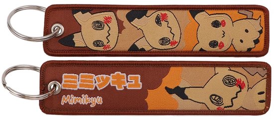 Porte-clés marron avec des figures Mimikyu marron et orange et du texte japonais.