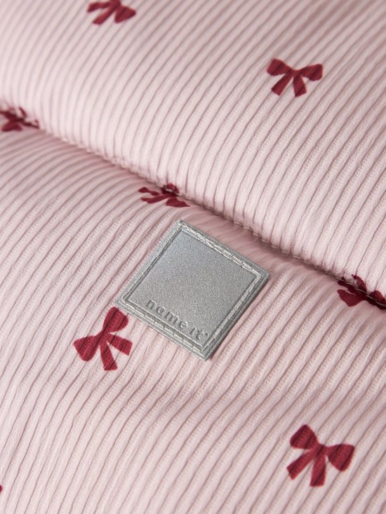 Detail van lichtroze, ribstof jas met donkerrode strikjesprint en merklabel.